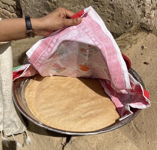 A wide bowl of bread is viewed under the raised corner of a cloth.