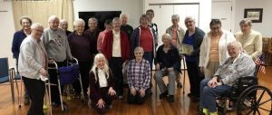 A diverse group of individuals sitting, standing, and crouching smiling together for a group photo indoors.