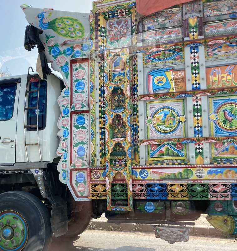A large white truck ornately decorated with a variety of images of birds, flowers and natural landscapes.