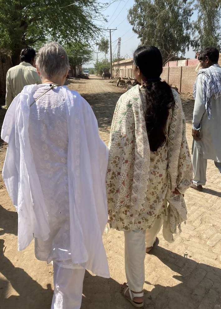 Two women and two men in Pakistani tunics walk down a dusty brick road.