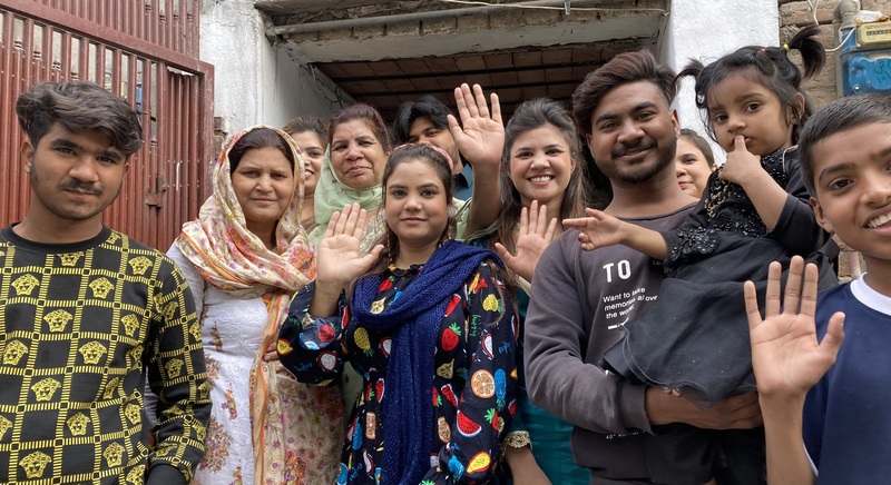 A large family group in Pakistan smiles and waves for the photo.