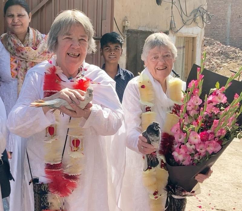 Two women in traditional Pakistani tunics hold pigeons and a huge bouquet of gladiolas.