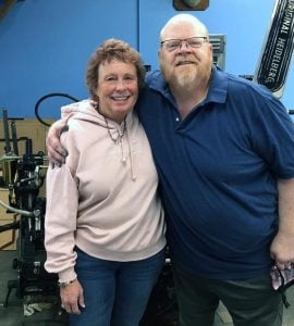 A man and women embracing one another and smiling for a photo next to a printing press.