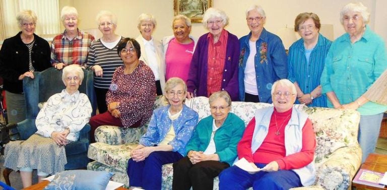A wide variety of individuals gathered together at an indoor community event smiling for a picture.