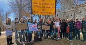 A large group of individuals collected outdoors for a photo with a sign saying, "Loretto Community honors the memory of Martin Luther King Jr.