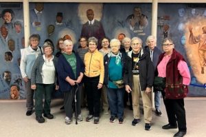 A group of women post for a photo in front of a mural depicting leaders of the American Civil Rights movement.