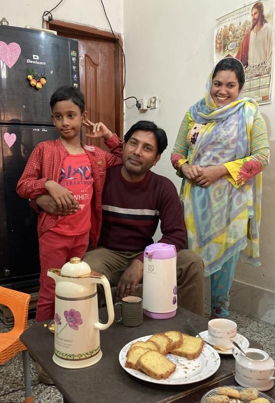 A Pakistani family - son, father and mother - pose together behind a table set for tea.