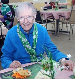 Short-haired woman with glasses smiling, wearing St. Patricks Day necklaces in a festive group dining room event.