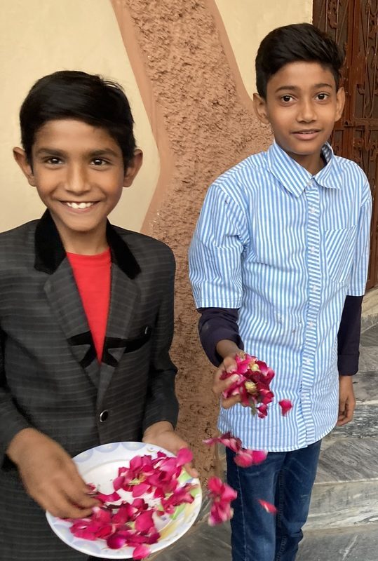 Two Pakistani boys stand with a plate and handfuls of rose petals.