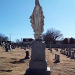 A blessed mother statue in a religious cemetery surrounded by 42 graves.