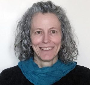 A smiling headshot of a curly haired woman with a blue scarf and a black blouse on.