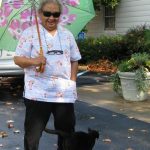 A woman wearing sunglasses with a floral umbrella on a sunny day with her cat outside.