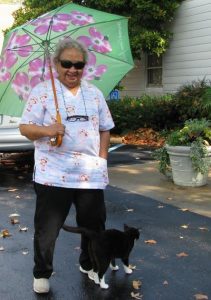 A woman wearing sunglasses with a floral umbrella on a sunny day with her cat outside.
