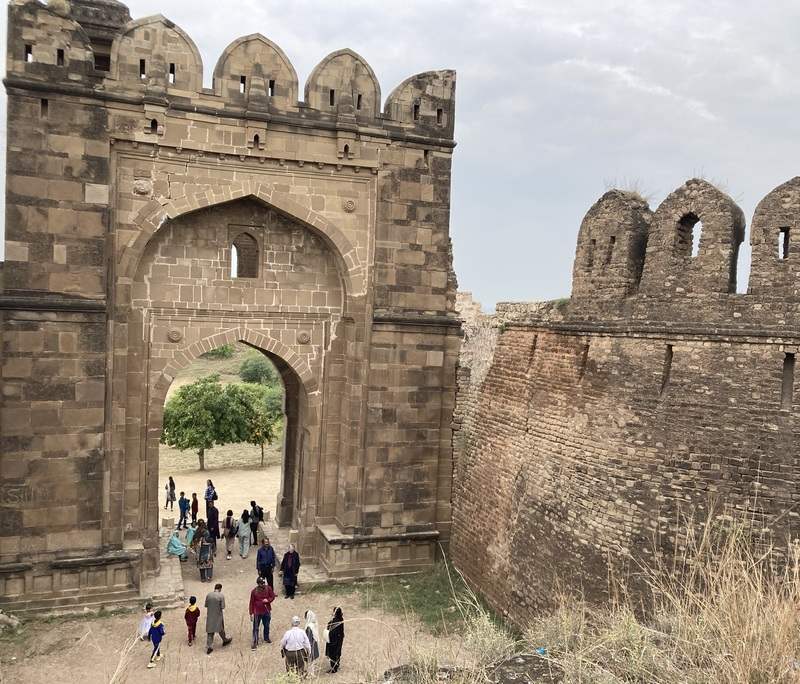 Twenty people tour the ruins of an old fort in Pakistan, crossing through a vaulted stone gate in the wall.