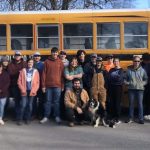 A group of young volunteers smiling together in front of a school bus.