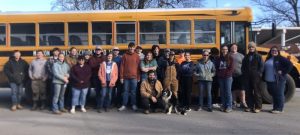 A group of young volunteers smiling together in front of a school bus.