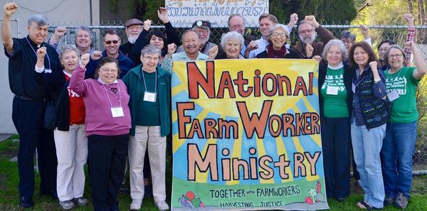 A farmworkers committee standing together outside with their fists in the air collectively holding a large, colorful sign that says National Farm Worker Ministry.