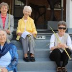 Five women sit on the steps of a porch, holding palms and smiling.