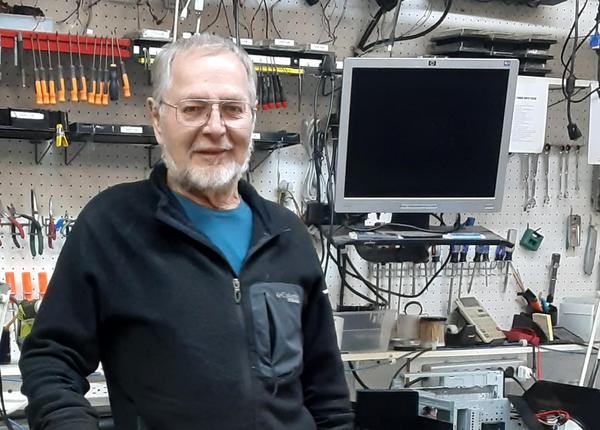 A bearded man standing in front of an electronics working station smiling for a photo.