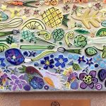 A colorful art piece with flower, veggie, and, fruit mosaics in a rainbow color pattering signifying all are welcome at the church.