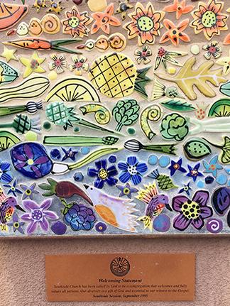A colorful art piece with flower, veggie, and, fruit mosaics in a rainbow color pattering signifying all are welcome at the church.