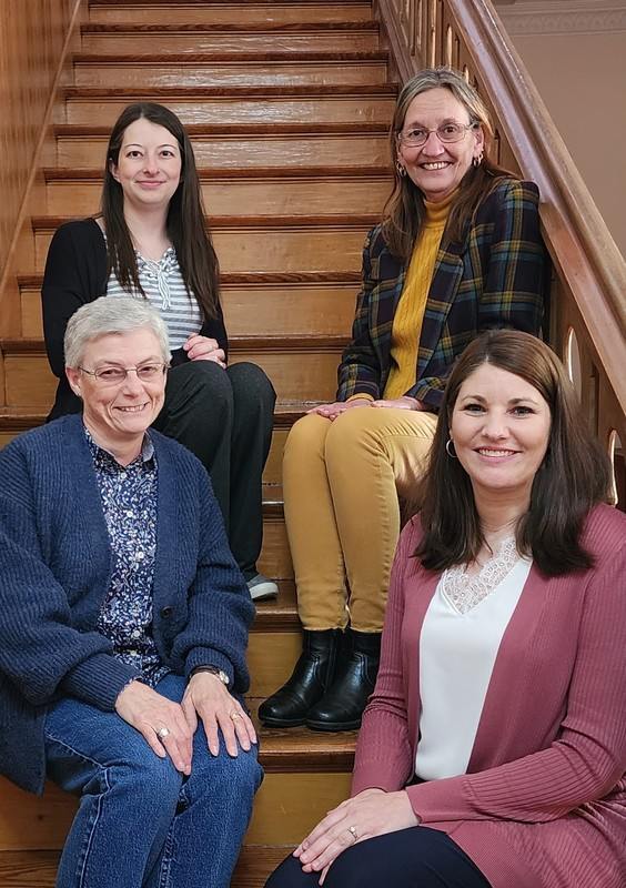 Four women smile for a photo, sitting on a wooden staircase.