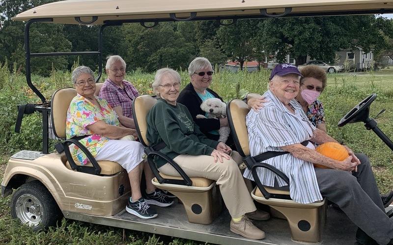 Six women smile from their seats on a golf cart.