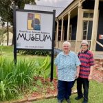 Two women smiling next to a museum sign outside.