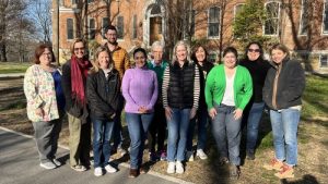 A wide variety of teachers all smile together for a group picture outside on a sunny day.