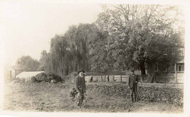 Black and white archival photo of two men standing by a large garden.