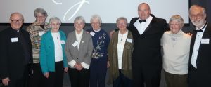9 diverse individuals smile for a group photo in dress clothes and name tags at an indoor event.