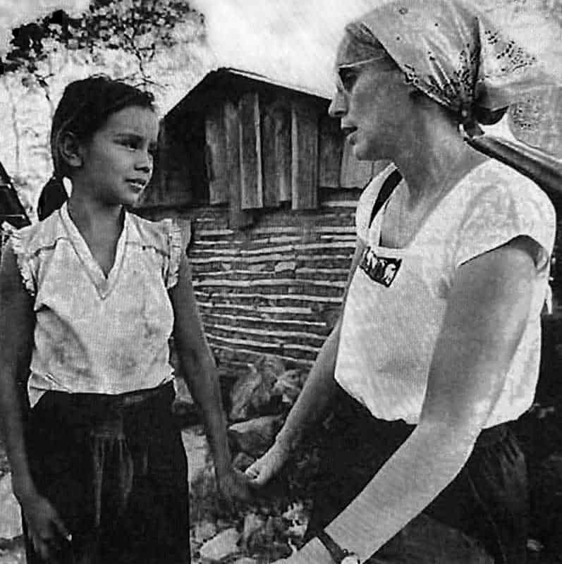 A woman holds a young girl's hand and talks with her.