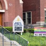The outside of a Saint Paul Catholic Church featuring a pride rainbow banner that says, 'LGBTQ+ Catholics Family, Friends, and Allies All are welcome.'