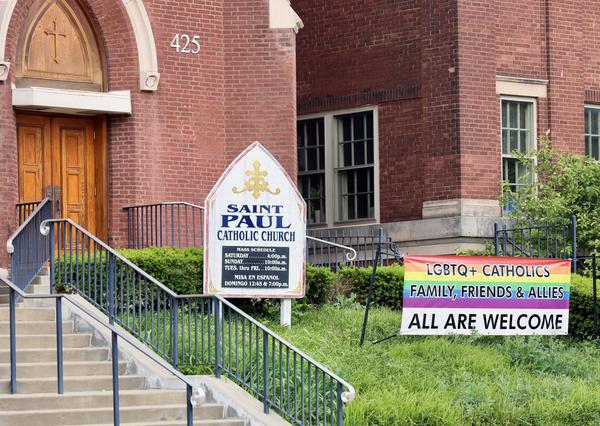 The outside of a Saint Paul Catholic Church featuring a pride rainbow banner that says, 'LGBTQ+ Catholics Family, Friends, and Allies All are welcome.'