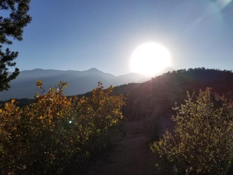 The sun beams over the tops of the mountains and trees.