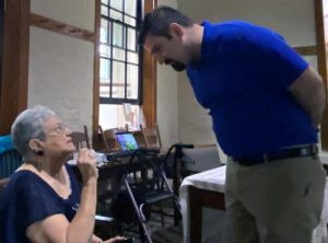 A man in a blue shirt standing over a short-haired woman having a conversation indoors.