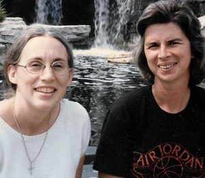 Two women pose for a photo together sitting in front of a waterfall.