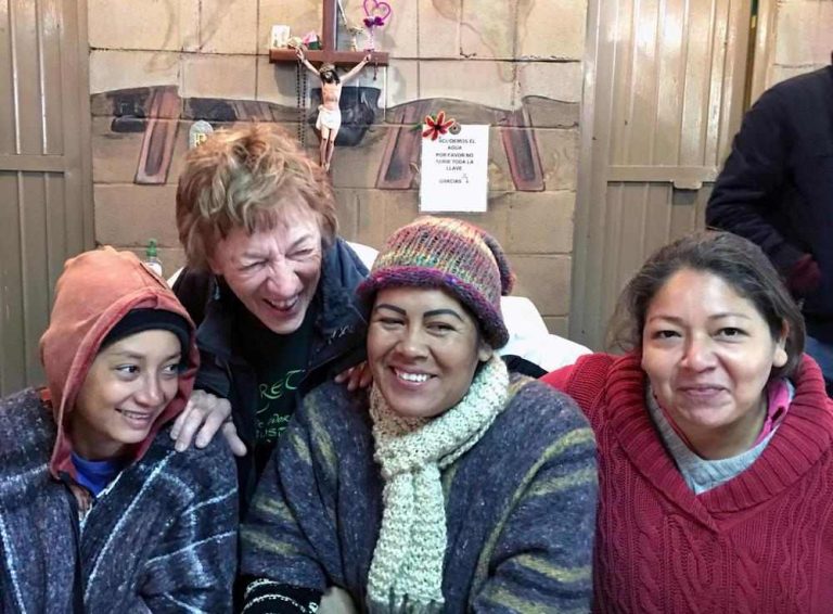 Four women, three Latinx and one White, dressed in warm clothes share a laugh together.