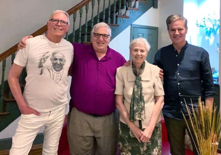 Three men and one woman smile together for a group picture in a house.
