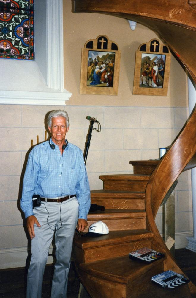 Man with a headset and filming gear smiles for a photo at the base of the circular staircase.