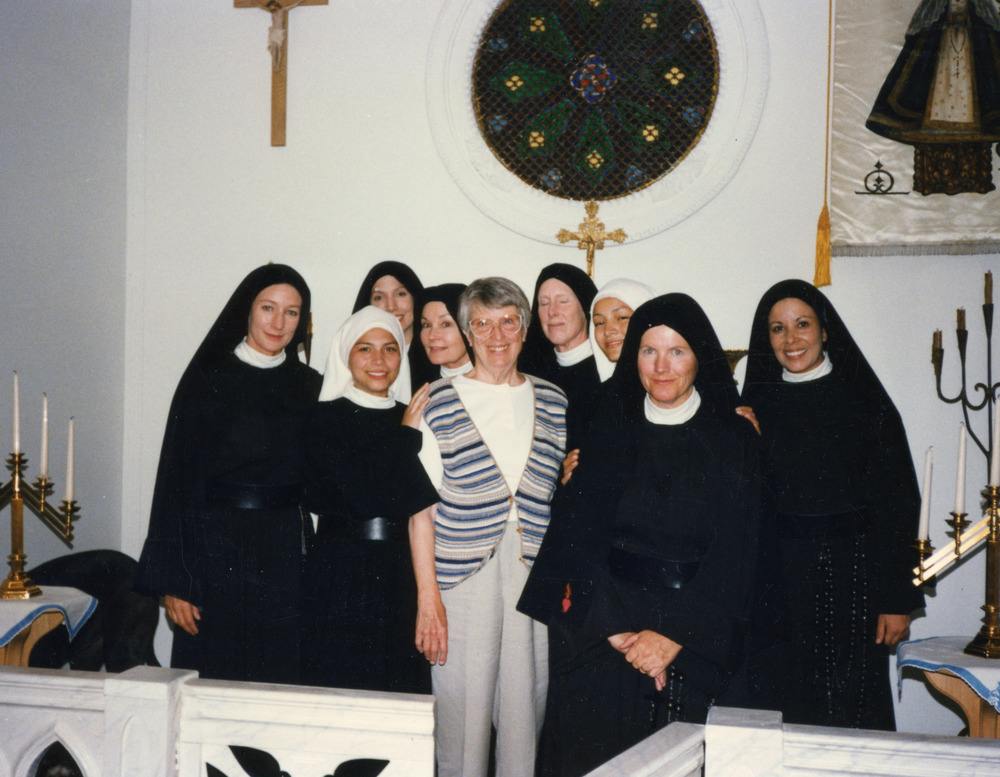 Women in habits pose for a photo around one woman in street clothes.