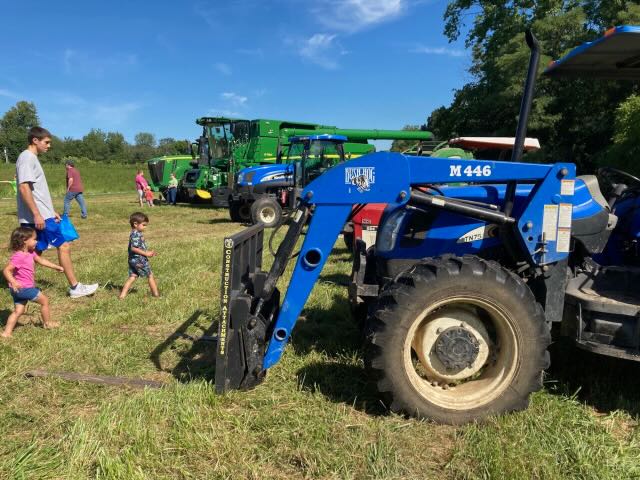 A man and two small children walk next to large green and blue tractors.