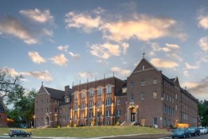 An historic, large brick building is profiled against the evening sky, lights twinkling brightly.
