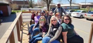 A group of teachers sitting on a farm hayride on a sunny day.