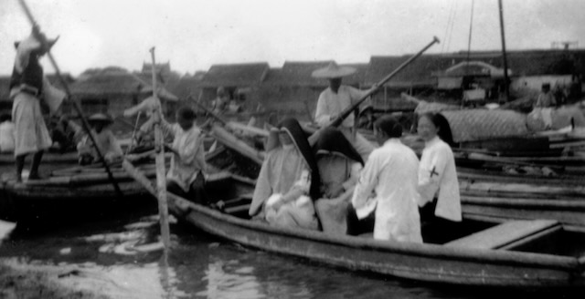 Black and white photo showing two sisters in habits and two medical professionals in white coats traveling by boat to deliver water and medicine after a flood.