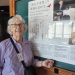 Woman stands next to a large framed poster in Japanese and English entitled "Towards a nuclear-free world"