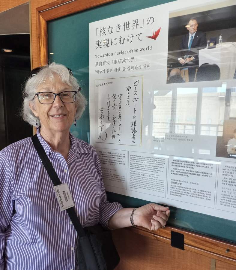 Woman stands next to a large framed poster in Japanese and English entitled "Towards a nuclear-free world"