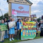 People hold signs at a Milk with Dignity rally in front of a Hannaford supermarket sign