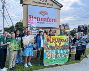 People hold signs at a Milk with Dignity rally in front of a Hannaford supermarket sign