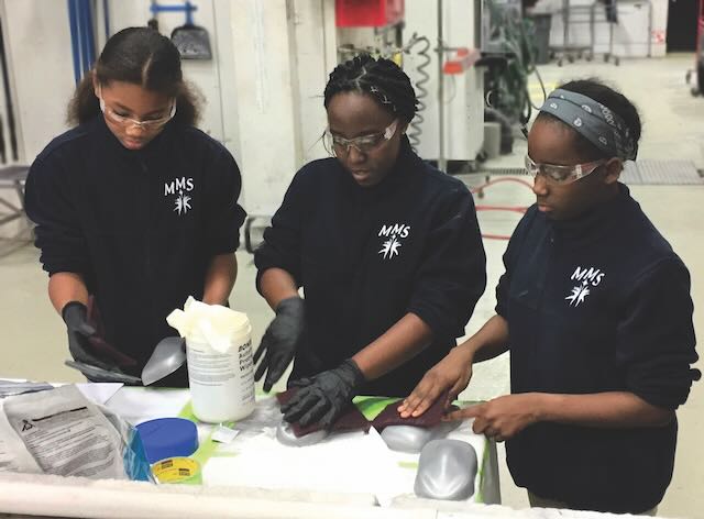 Three middle schoolers with safety googles collaborate on a science project together.